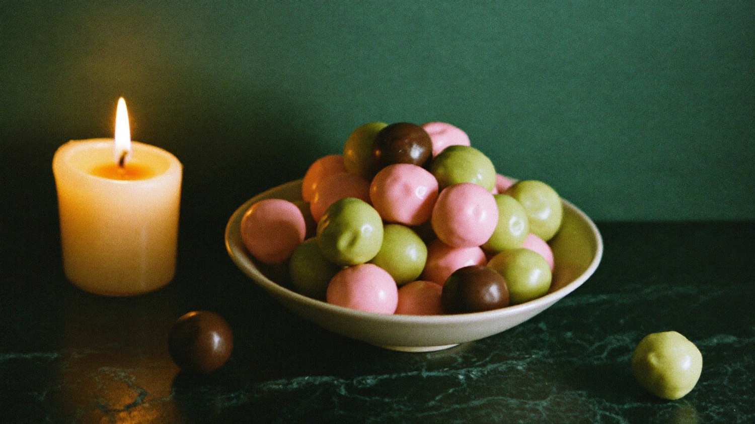 Bunte LAKRIDS-Lakritzkugeln in Rosa, Grün und Braun in einer Keramikschale im Kerzenlicht