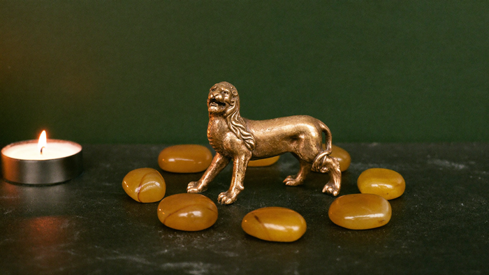 Messing-Löwenfigur umringt von acht Bernsteinen im Kerzenlicht — Symbolbild für das Löwentor am 8.8.2026