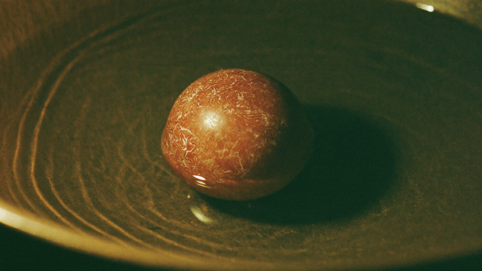 Rostrote Steinkugel in einer flachen Schale mit stillem Wasser im warmen Kerzenlicht