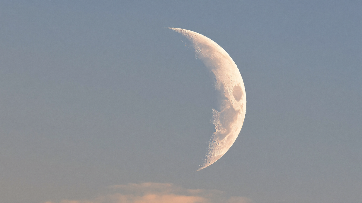 Schmale Mondsichel am hellen blassblauen Taghimmel, Krater entlang der Lichtgrenze sichtbar