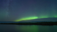 Nachtlandschaft an einer flachen norddeutschen Küste, über dem Nordhorizont ein niedriger grüner Polarlichtbogen, darüber Sternenhimmel