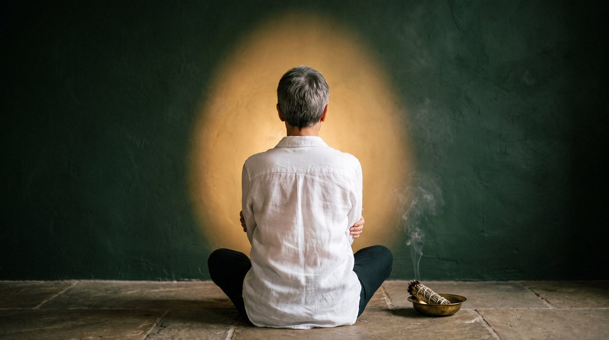 Person von hinten im Meditationssitz mit vor der Brust gekreuzten Armen vor warmem Lichtschein – psychischer Selbstschutz und Aura