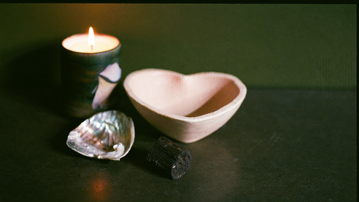 Herzförmige Keramikschale, Abalone-Muschel und Palo Santo Holz auf dunklem Stein neben einer brennenden Kerze