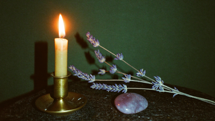Brennende Kerze im Messinghalter mit getrocknetem Lavendel und Amethyst