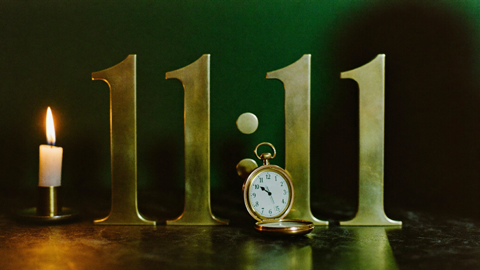 Große Messingziffern 11:11 vor einer dunkelgrünen Wand, davor eine geöffnete Taschenuhr, links eine brennende Kerze – Titelbild zu allen Spiegelstunden