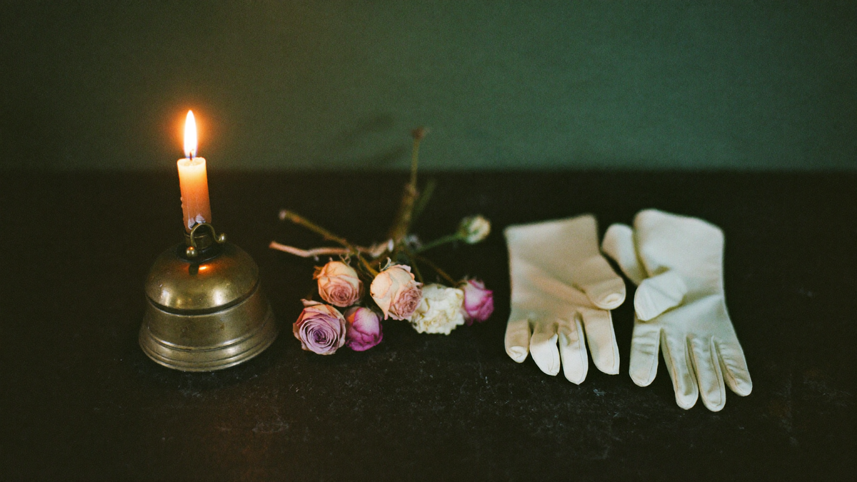 Séance-Stillleben: Messingglocke, weiße Handschuhe und getrocknete Rosen im Kerzenlicht