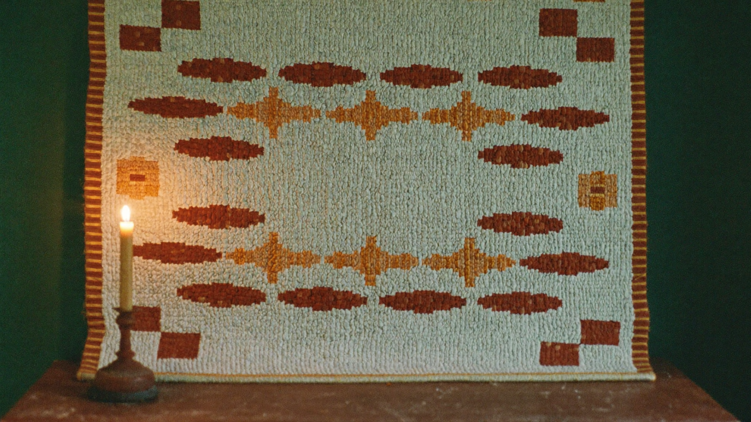 Gewebtes Kilim-Muster in Mint, Rostbraun und Gold als Wandbehang im Kerzenlicht
