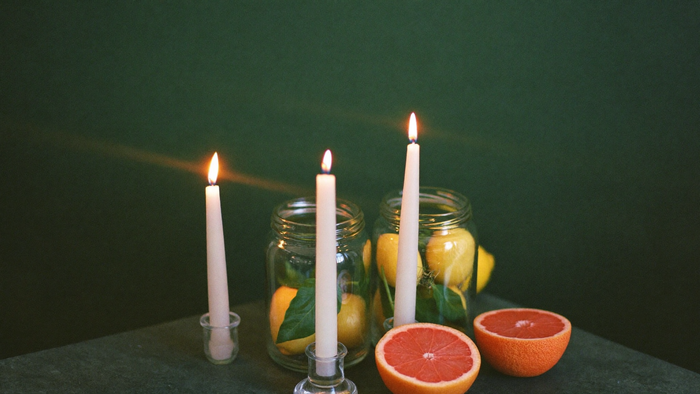 Brennende Kerzen mit Zitronen und halbierter Grapefruit vor dunkelgrüner Wand