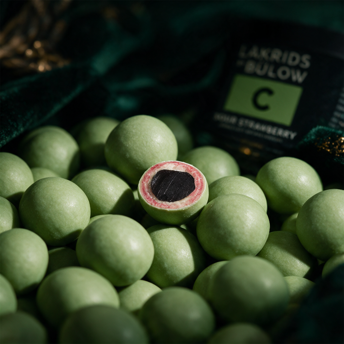 LAKRIDS by BÃ¼low Sour Strawberry | Lakritz in weiÃŸer Schokolade â€“ Detailansicht vor tiefem SmaragdgrÃ¼n