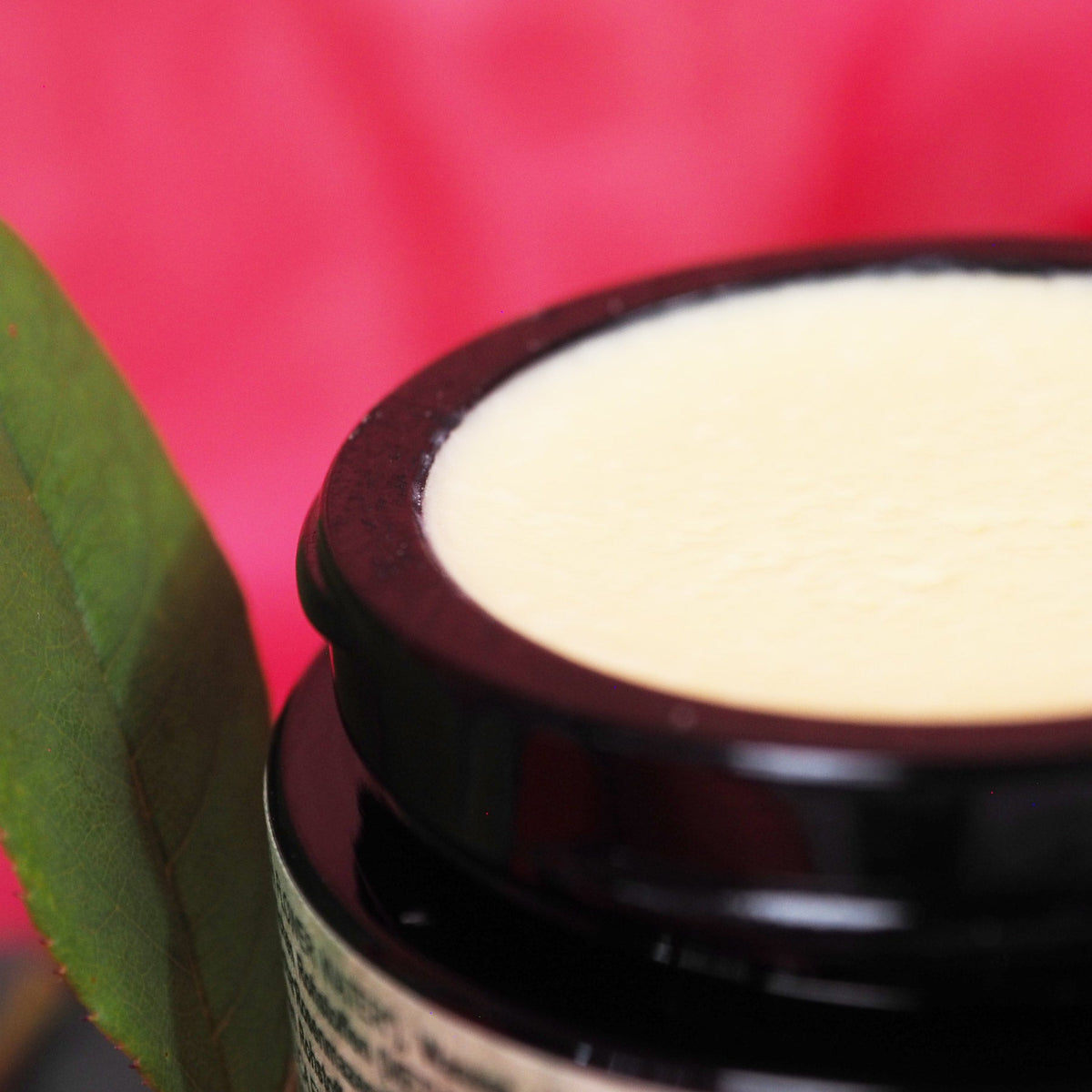 Nahaufnahme der cremeweißen Textur der Rosa Alchemystica Creme im dunklen Glastiegel