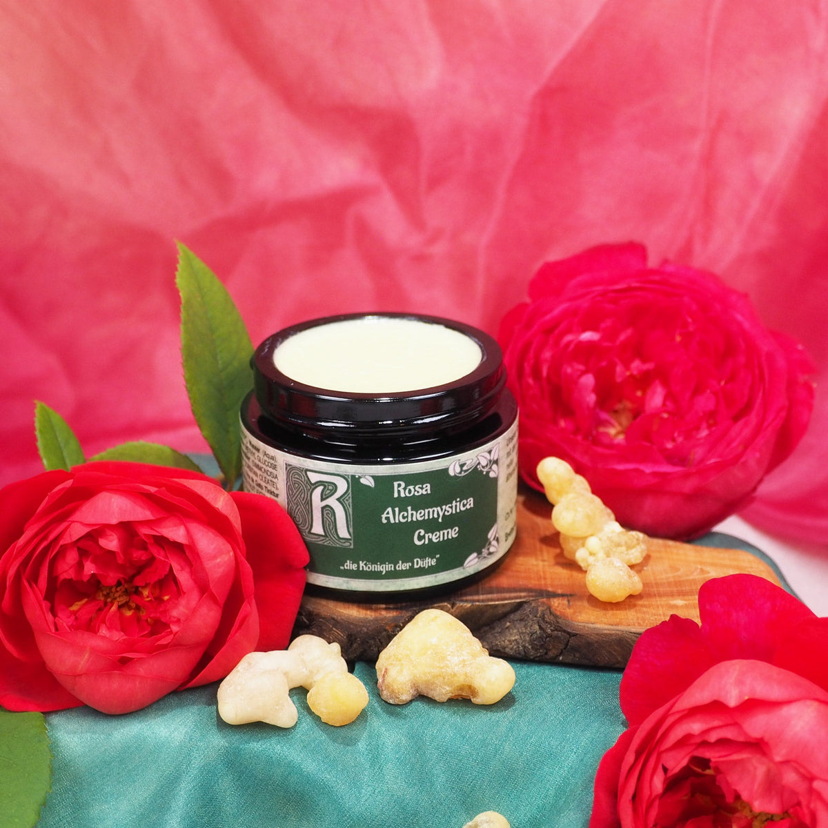 Offener Tiegel Rosa Alchemystica Creme auf einem Holzbrett zwischen roten Rosen und Weihrauchharz