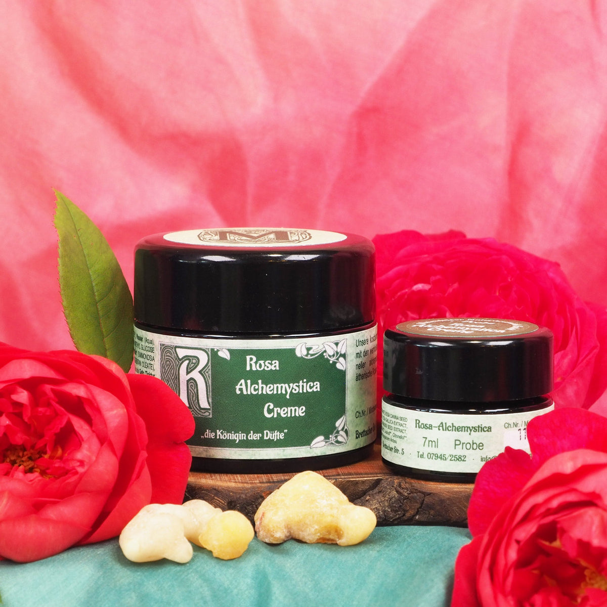 Rosa Alchemystica Creme von Maienfelser im 35-ml-Tiegel und als 7-ml-Probe, umgeben von roten Rosen und Weihrauchharz