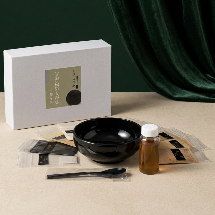 Inhalt des Nerikō-Sets: schwarze Anrührschale, schwarzer Löffel, Fläschchen mit bernsteinfarbener Flüssigkeit und Beutel mit Duftmaterialien