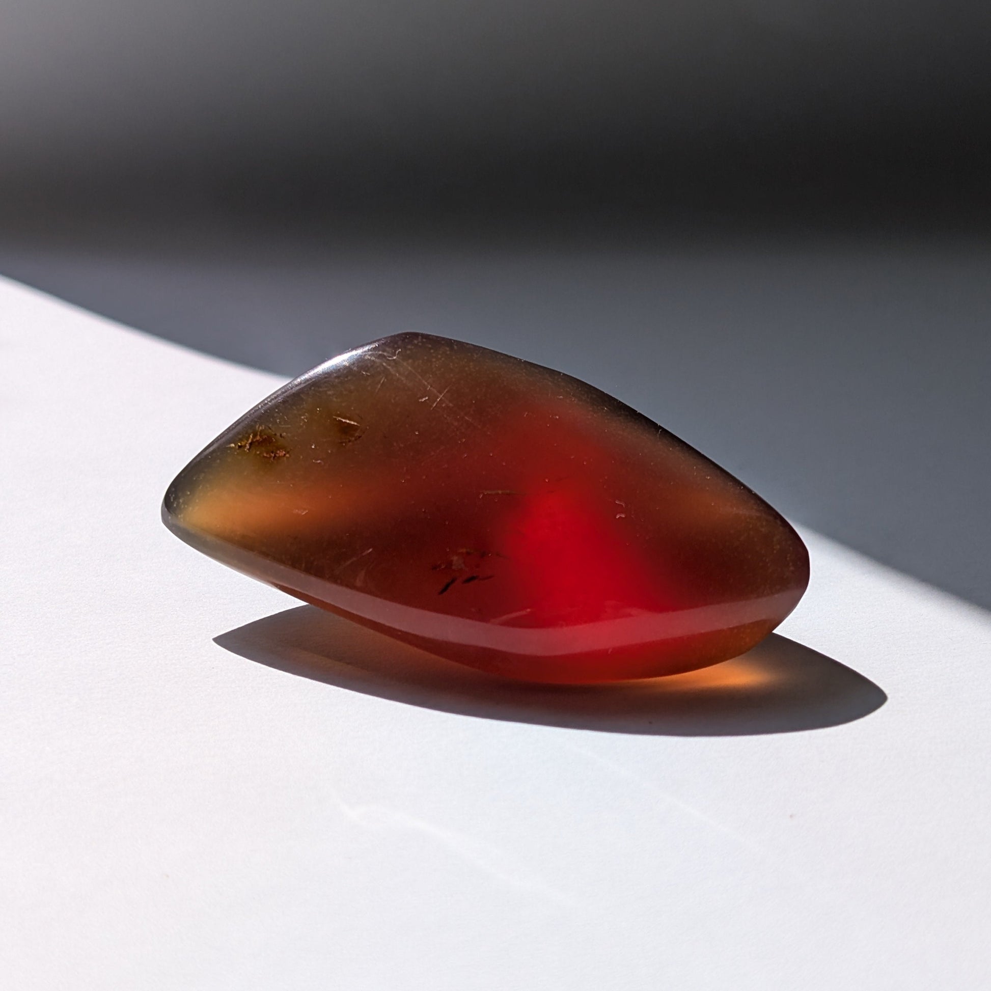 Bernstein Talisman "Funke der Vorzeit" in dunkler, tropfenartiger Form mit rotem Kern.
