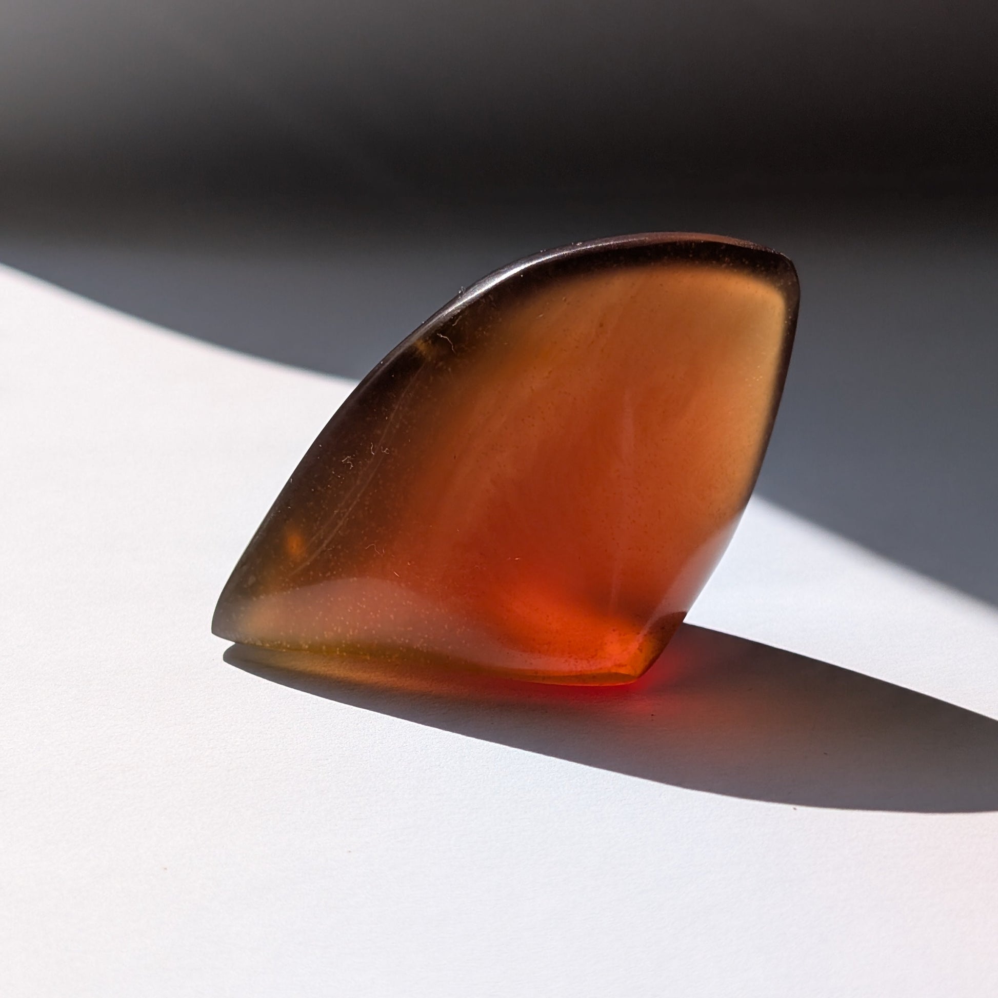 Bernstein Talisman "Funke der Vorzeit" in dunkler, tropfenartiger Form mit rotem Kern.