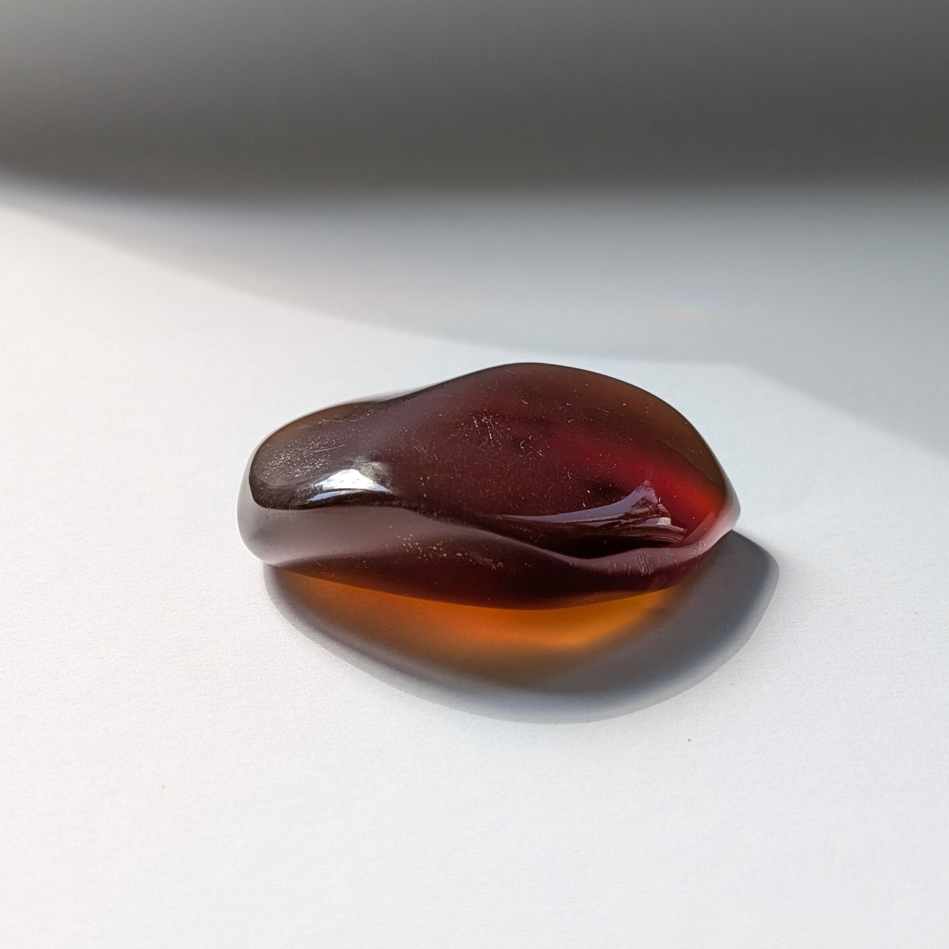 Bernstein Talisman "Tropfen der Vorzeit" in dunkler, tropfenartiger Form mit rotem Kern.