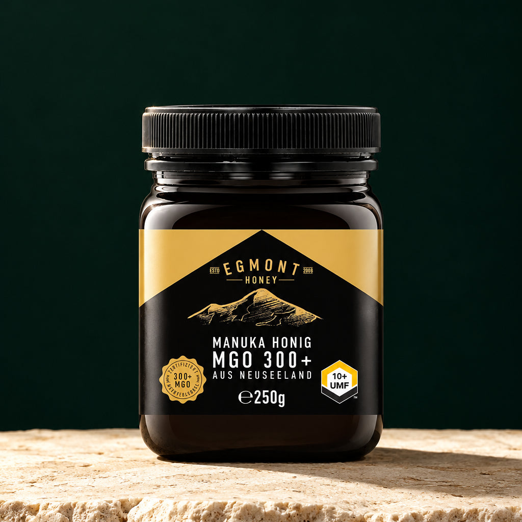 Glas Egmont Honey Manuka Honig MGO 300+ 250 g auf hellem Stein vor dunkelgrünem Hintergrund
