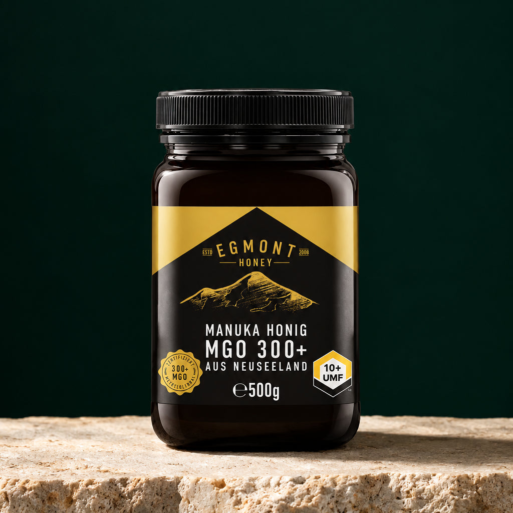 Glas Egmont Honey Manuka Honig MGO 300+ 500 g auf hellem Stein vor dunkelgrünem Hintergrund