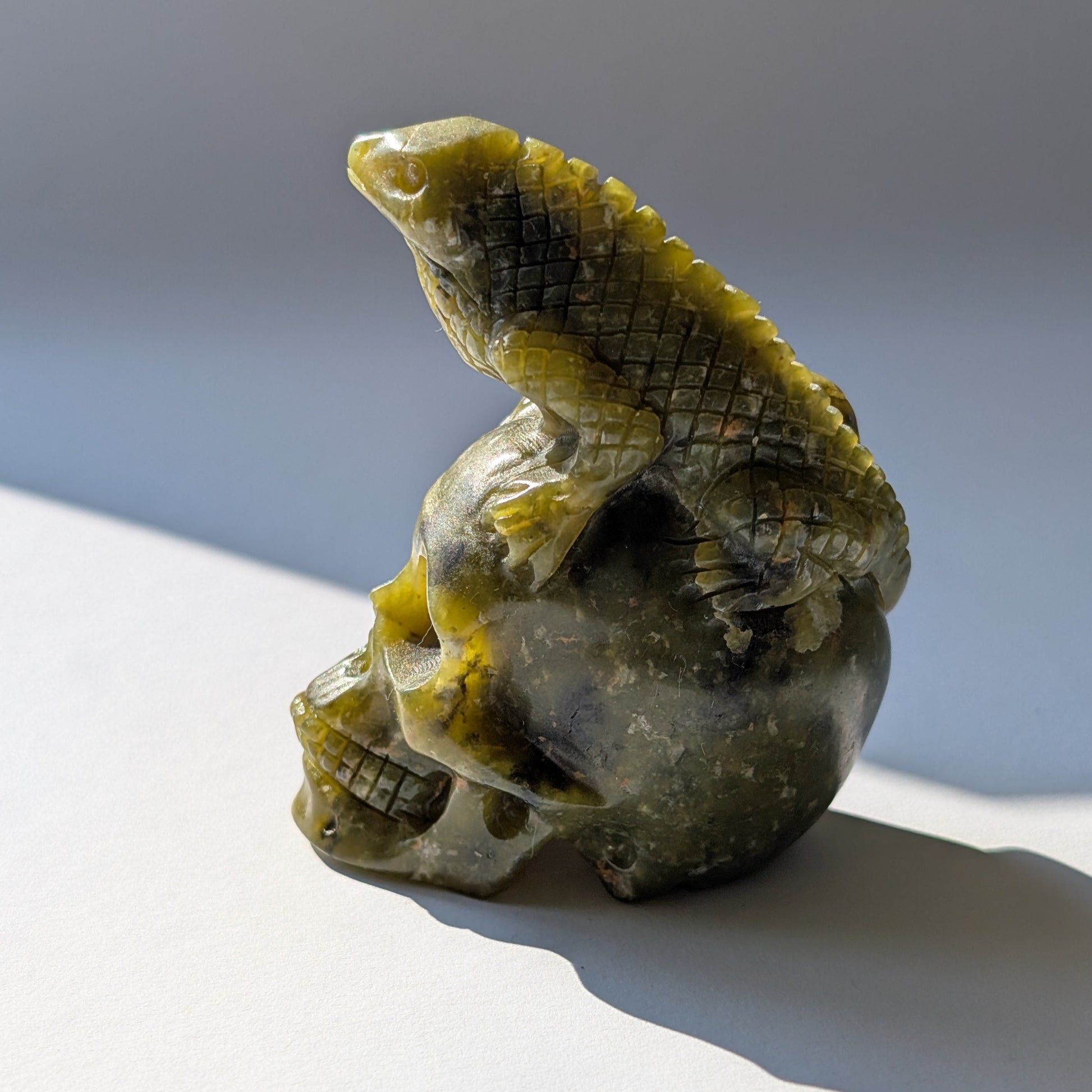 Ein 168g schwerer, handgeschnitzter Kristallschädel 'Veratha' aus grünem Serpentin, mit einer detailreichen Kobra, die sich auf seinem Scheitel aufrichtet.