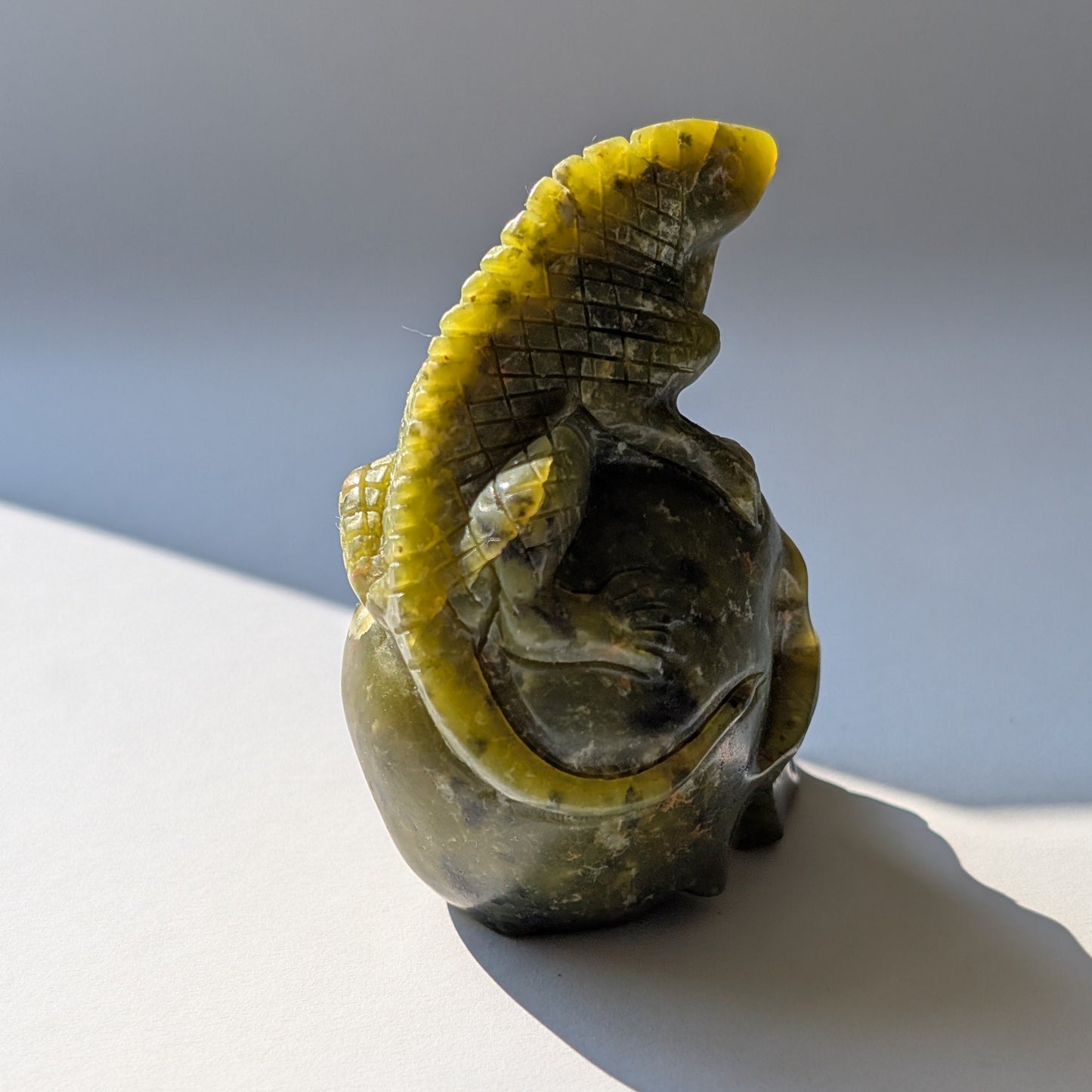Ein 168g schwerer, handgeschnitzter Kristallschädel 'Veratha' aus grünem Serpentin, mit einer detailreichen Kobra, die sich auf seinem Scheitel aufrichtet.