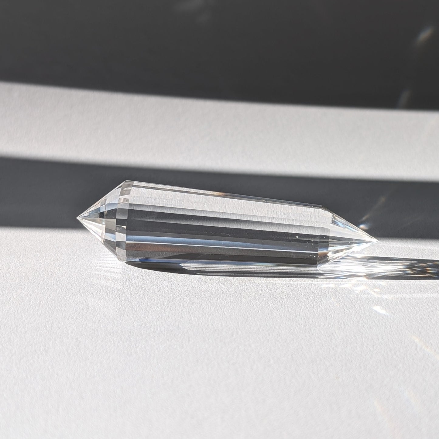 Ein 24-Facetten Vogel-Kristall aus wasserklarem Bergkristall, liegend im Sonnenlicht, das sich in ihm bricht.