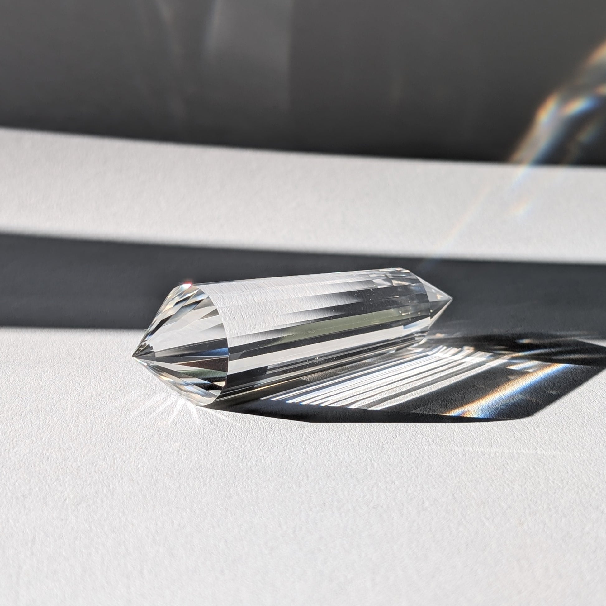 Ein 24-Facetten Vogel-Kristall aus wasserklarem Bergkristall, liegend im Sonnenlicht, das sich in ihm bricht.