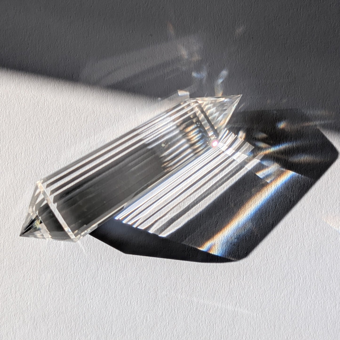 Ein 24-Facetten Vogel-Kristall aus wasserklarem Bergkristall, liegend im Sonnenlicht, das sich in ihm bricht.