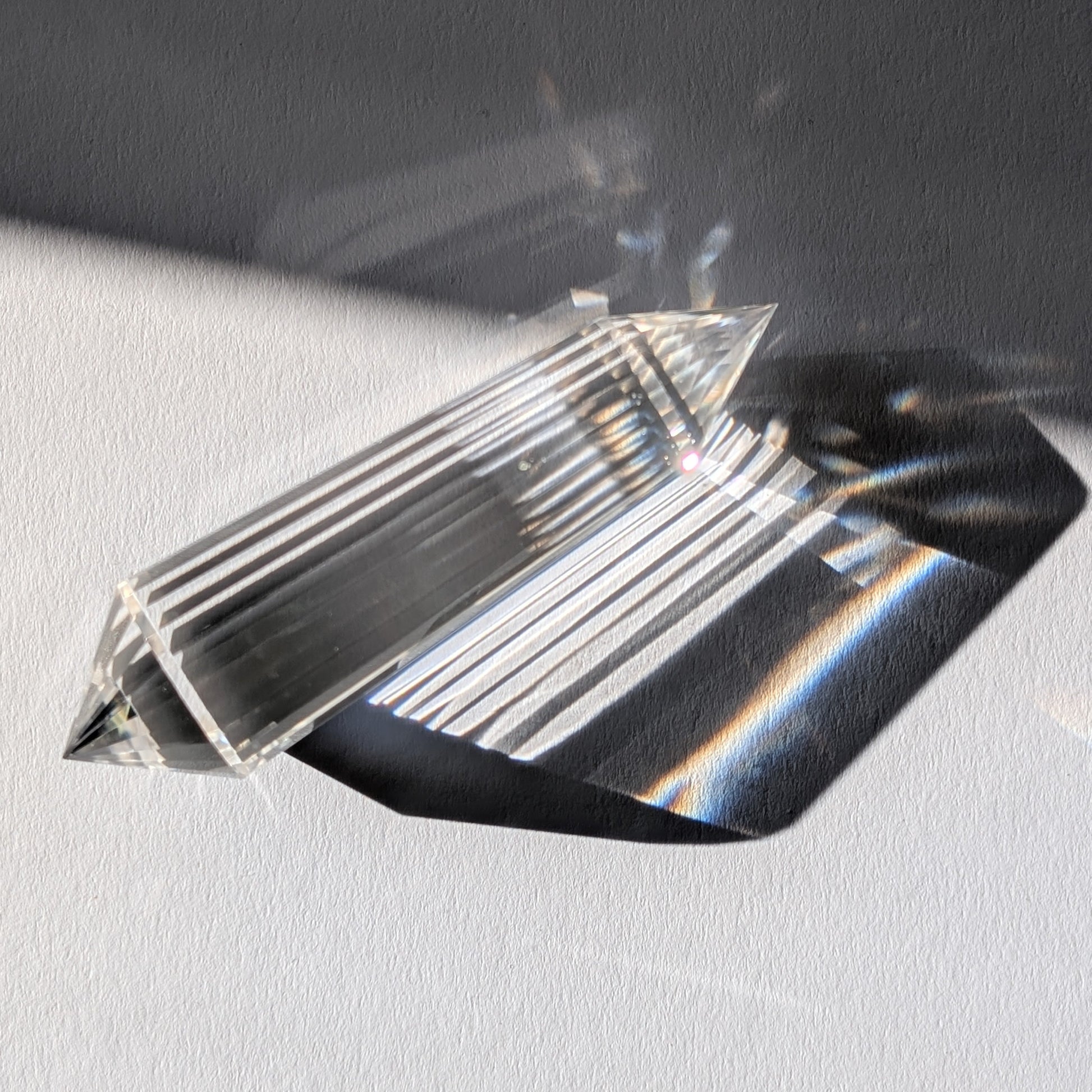 Ein 24-Facetten Vogel-Kristall aus wasserklarem Bergkristall, liegend im Sonnenlicht, das sich in ihm bricht.