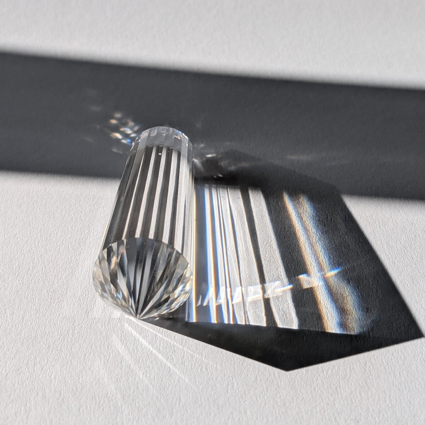 Ein 24-Facetten Vogel-Kristall aus wasserklarem Bergkristall, liegend im Sonnenlicht, das sich in ihm bricht.