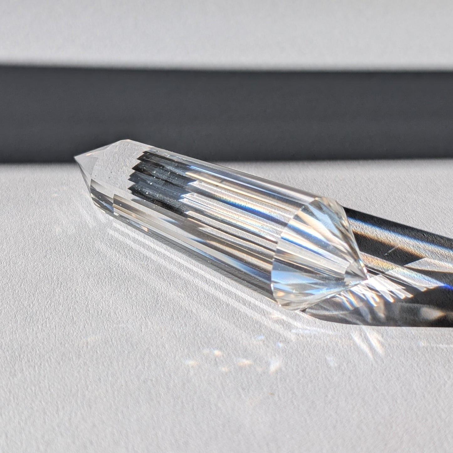 Ein 24-Facetten Vogel-Kristall aus wasserklarem Bergkristall, liegend im Sonnenlicht, das sich in ihm bricht.