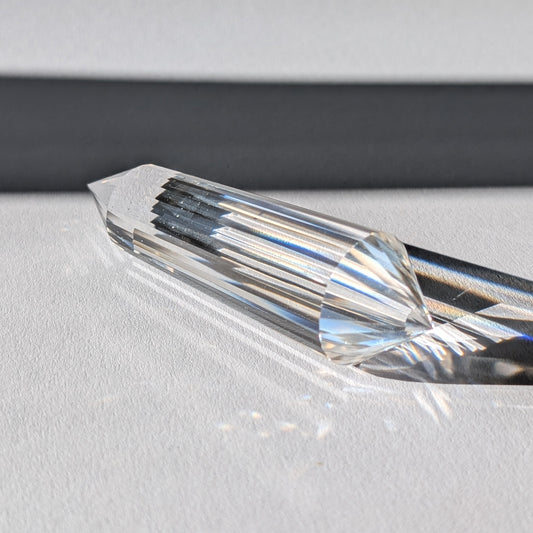 Ein 24-Facetten Vogel-Kristall aus wasserklarem Bergkristall, liegend im Sonnenlicht, das sich in ihm bricht.