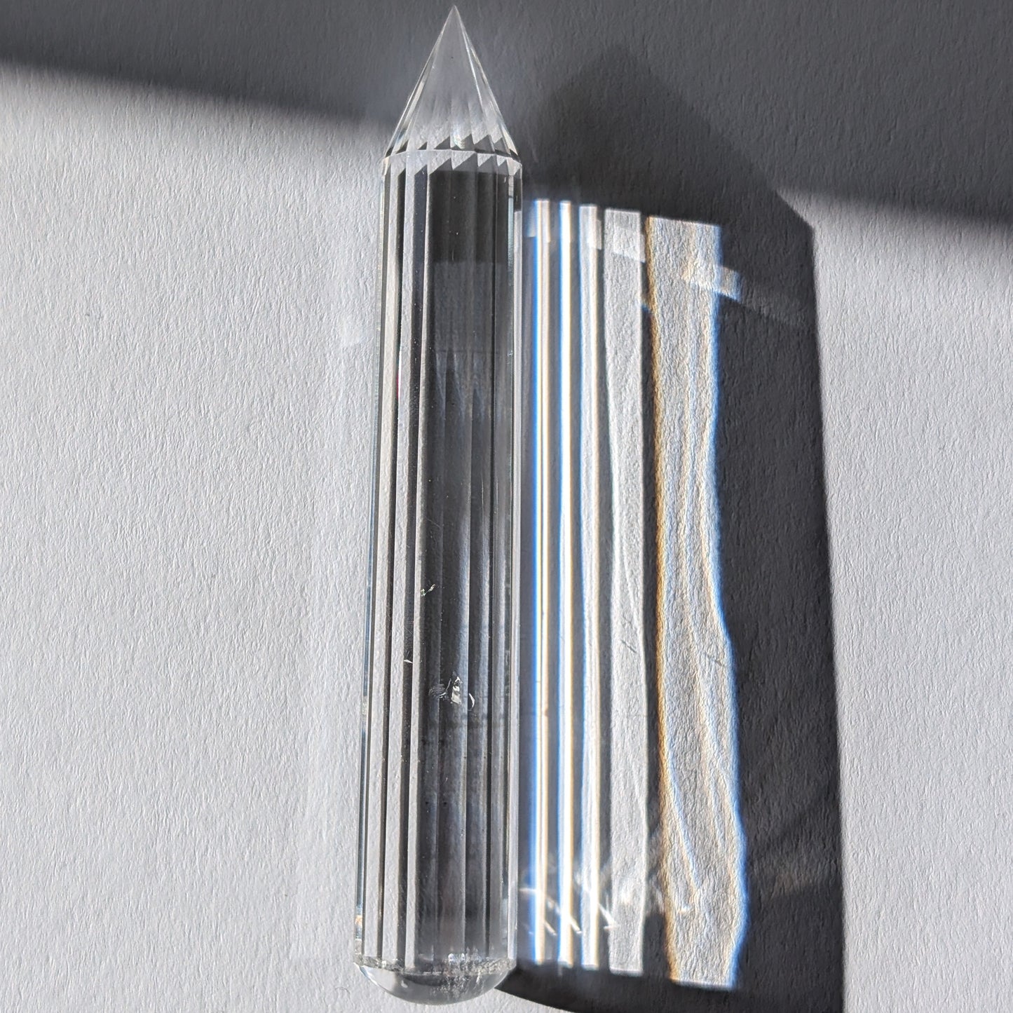 Ein 24-fach gerillter (fluted) Heilerstab aus wasserklarem Bergkristall (50g), der Licht reflektiert.