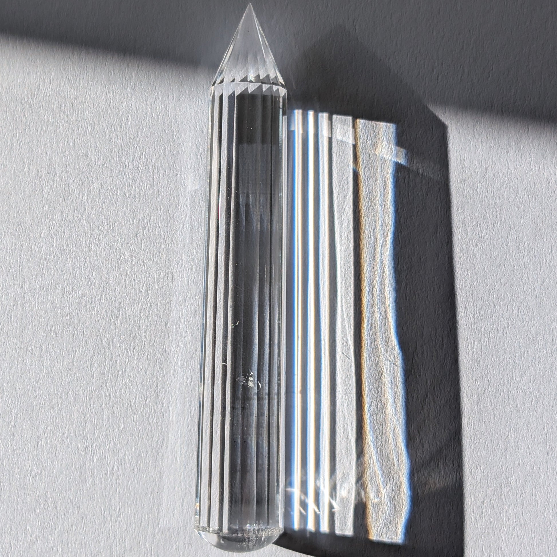 Ein 24-fach gerillter (fluted) Heilerstab aus wasserklarem Bergkristall (50g), der Licht reflektiert.