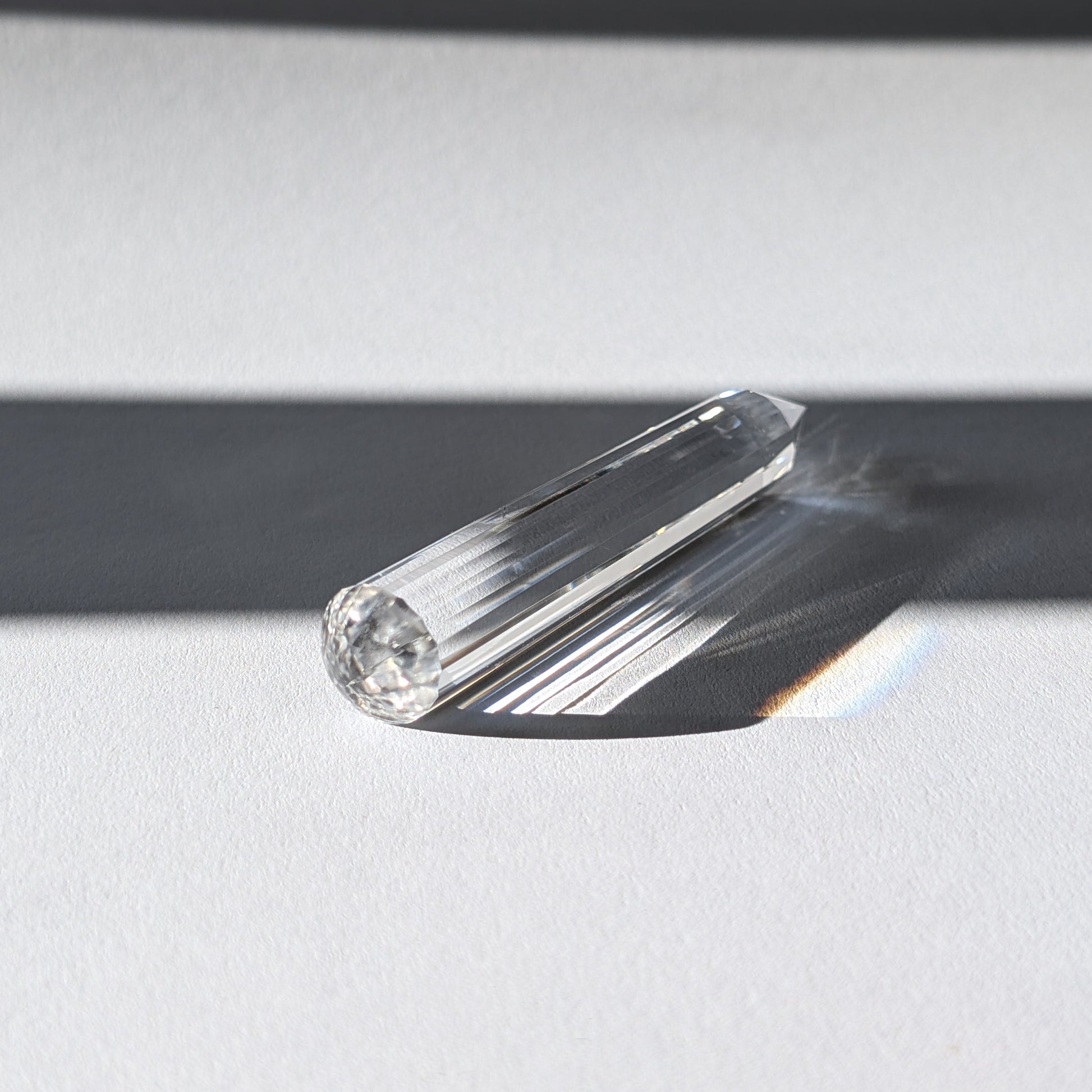 Ein 24-fach gerillter (fluted) Heilerstab aus wasserklarem Bergkristall (50g), der Licht reflektiert.