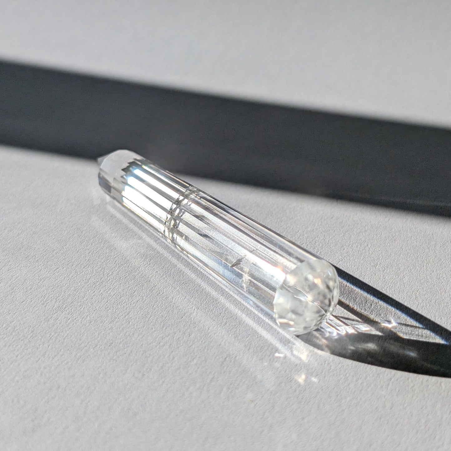 Ein 24-fach gerillter (fluted) Heilerstab aus wasserklarem Bergkristall (59g) im Licht.