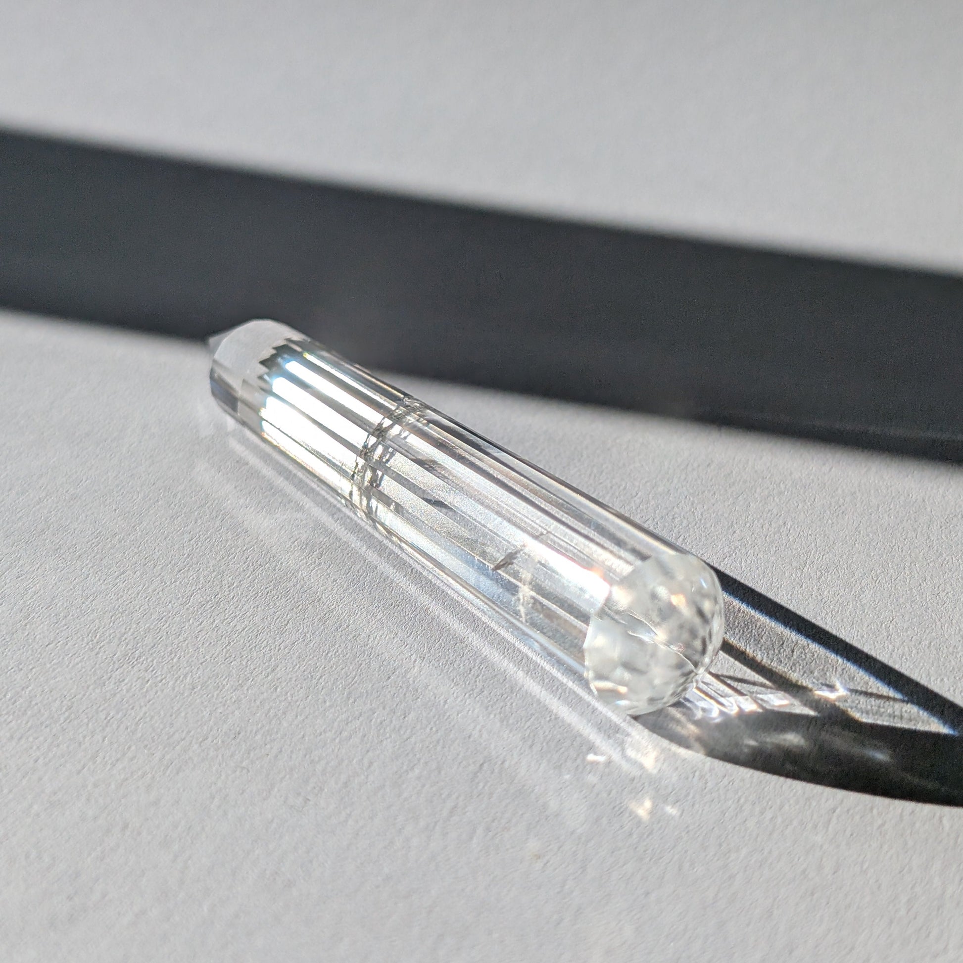 Ein 24-fach gerillter (fluted) Heilerstab aus wasserklarem Bergkristall (59g) im Licht.