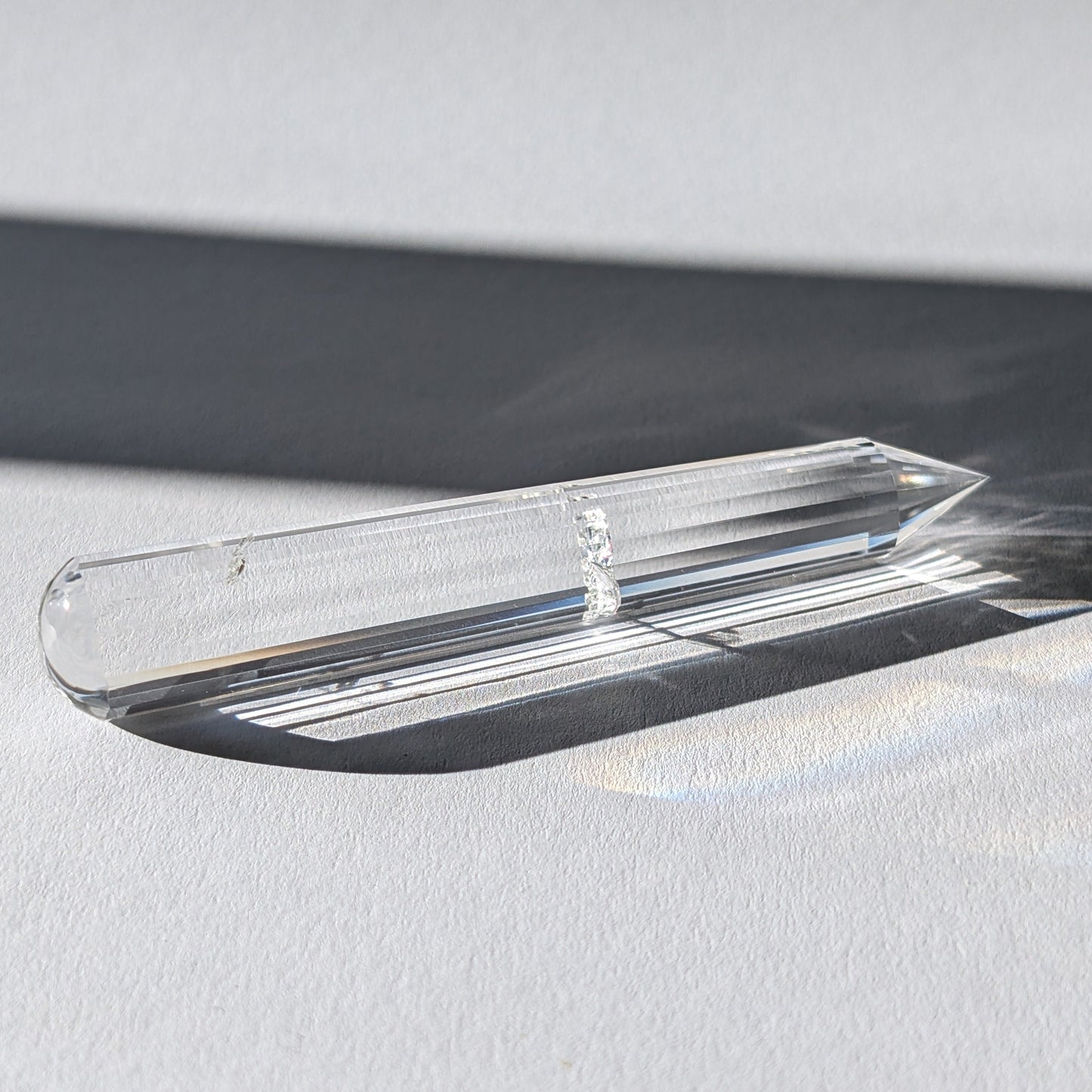 Ein 24-fach gerillter (fluted) Heilerstab aus wasserklarem Bergkristall (59g) im Licht.