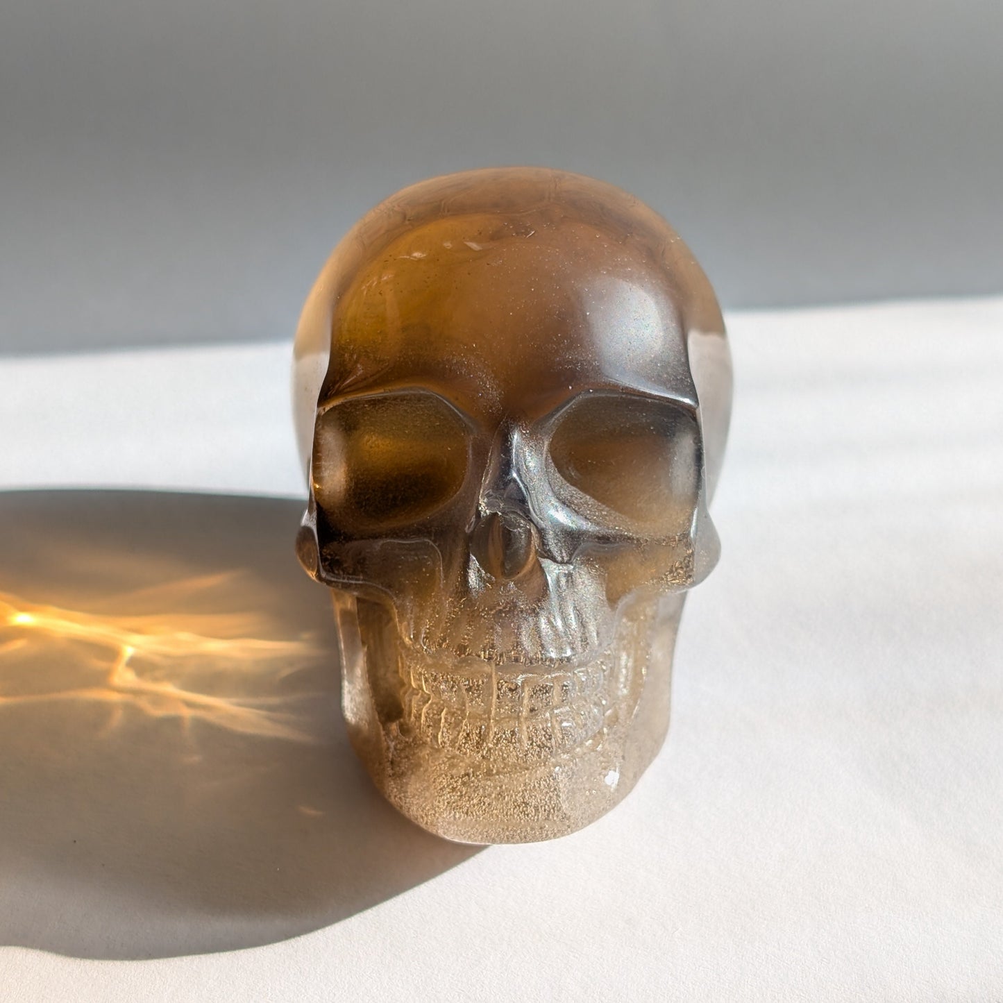 Ein 258g schwerer, synthetischer Rauchquarz-Schädel 'Auric' mit unzähligen goldenen Partikeln, die wie Sternenstaub im Licht funkeln.