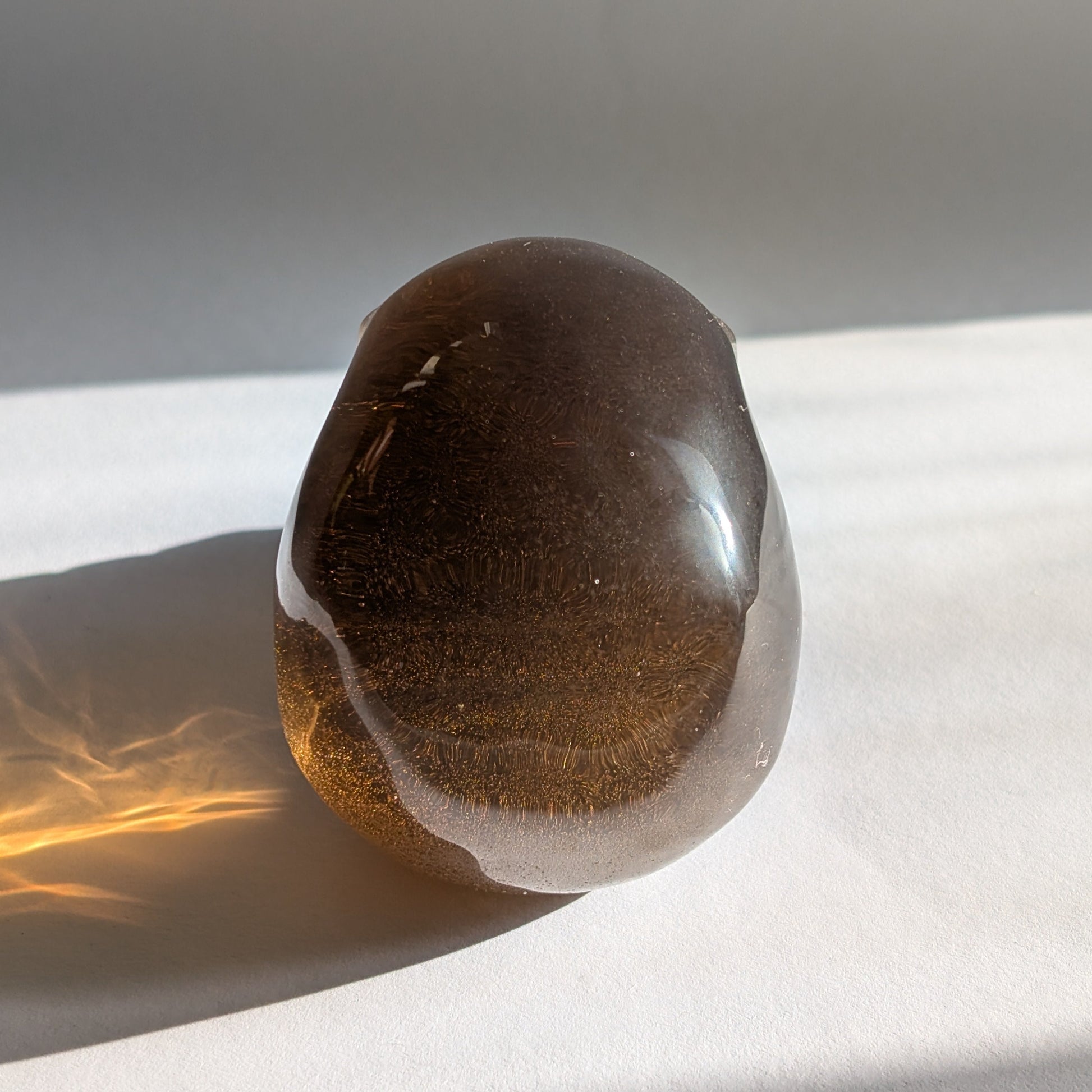 Ein 258g schwerer, synthetischer Rauchquarz-Schädel 'Auric' mit unzähligen goldenen Partikeln, die wie Sternenstaub im Licht funkeln.