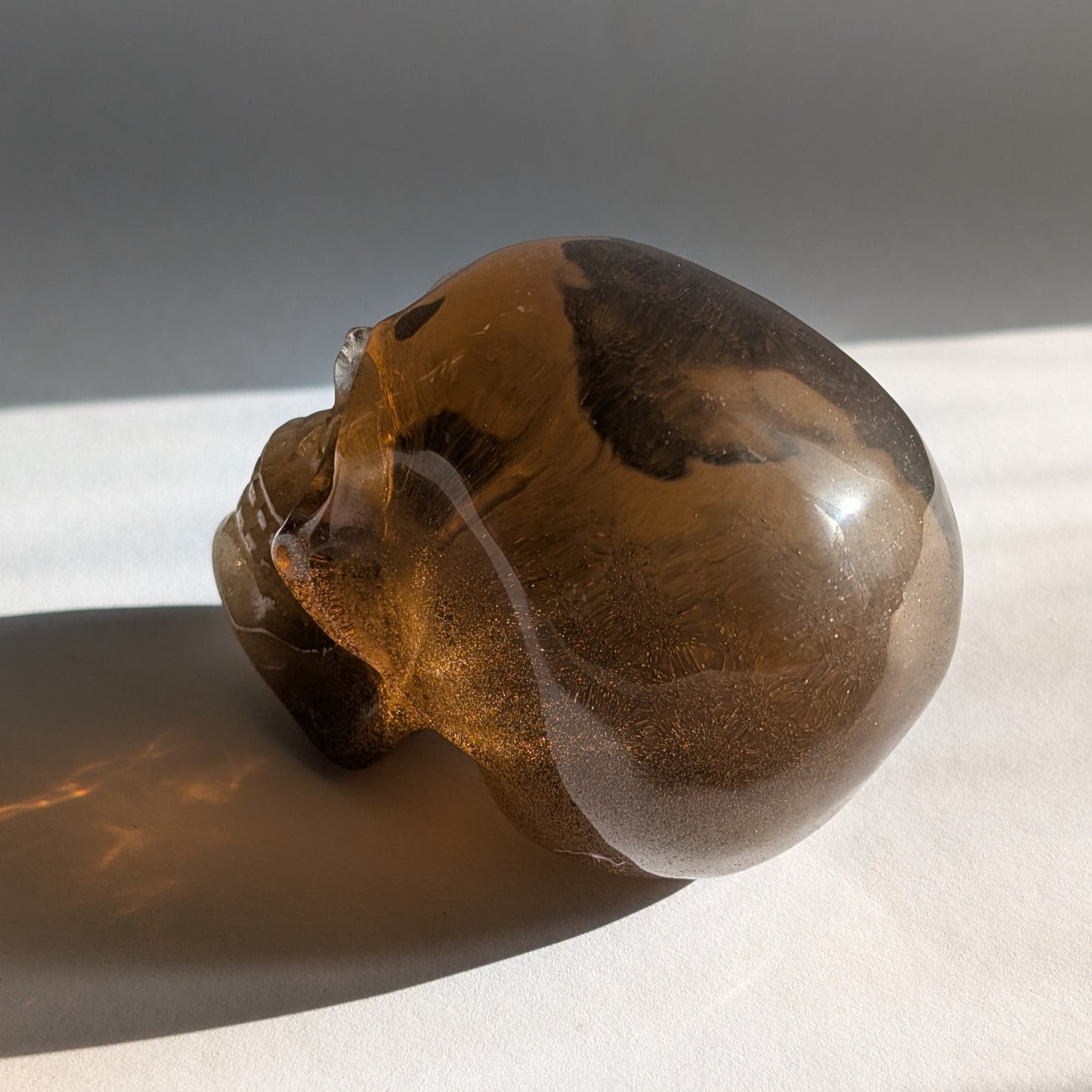 Ein 258g schwerer, synthetischer Rauchquarz-Schädel 'Auric' mit unzähligen goldenen Partikeln, die wie Sternenstaub im Licht funkeln.