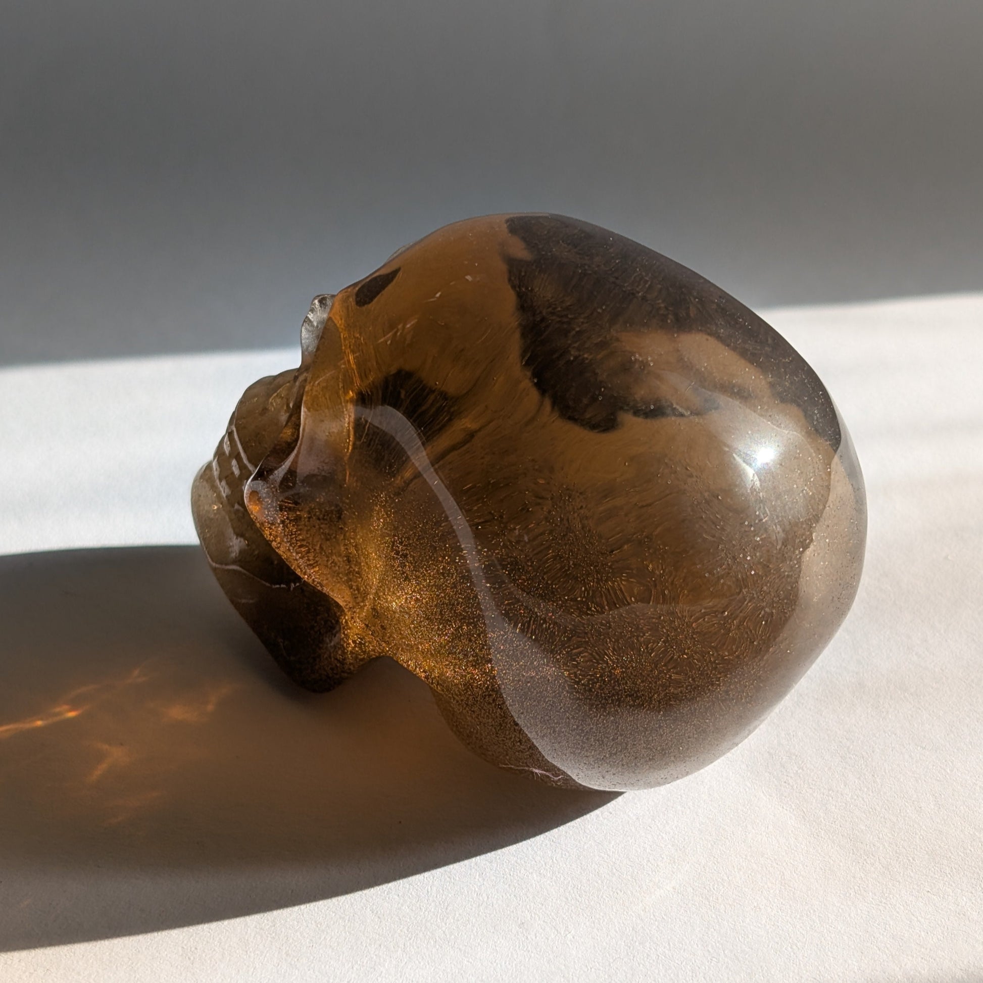 Ein 258g schwerer, synthetischer Rauchquarz-Schädel 'Auric' mit unzähligen goldenen Partikeln, die wie Sternenstaub im Licht funkeln.
