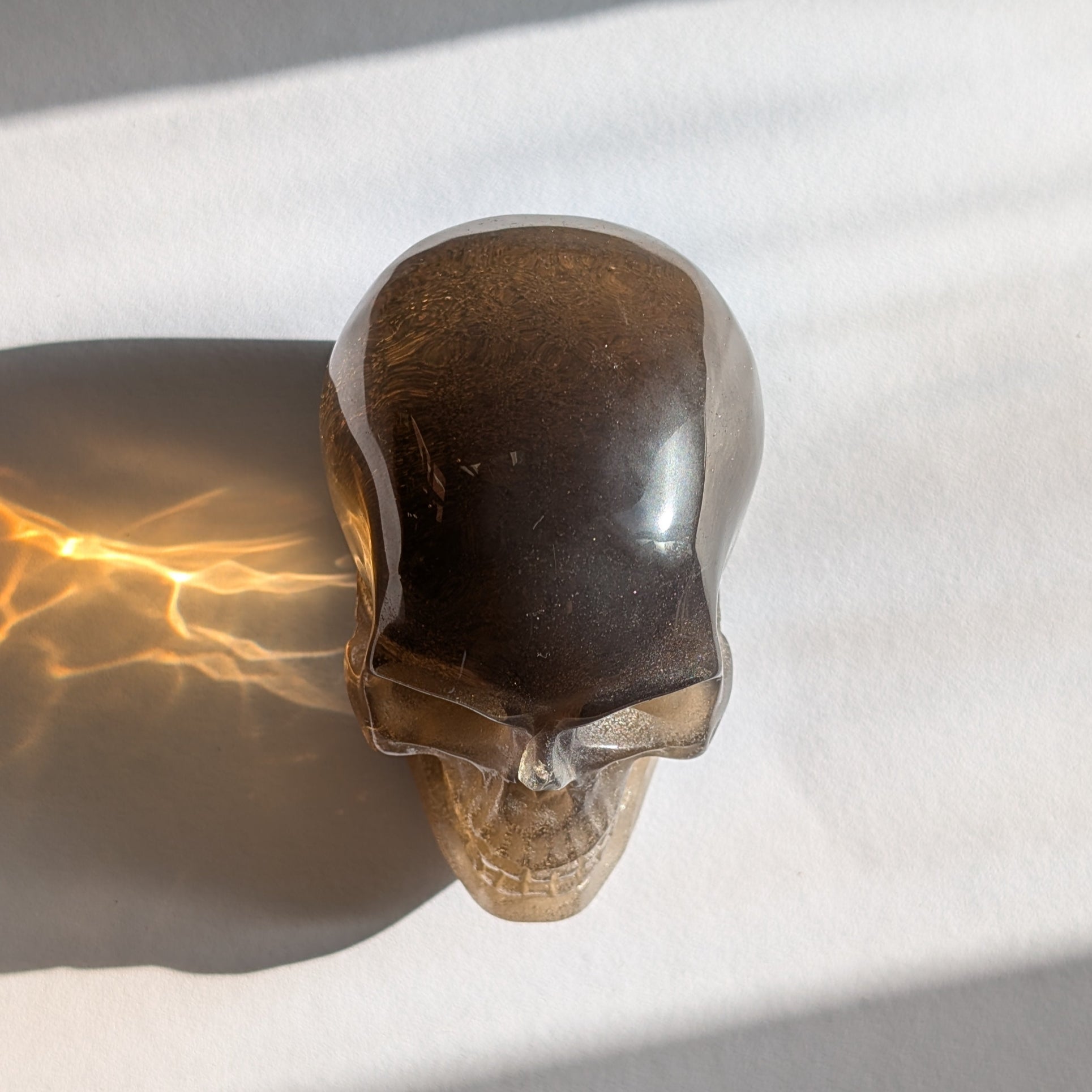 Ein 258g schwerer, synthetischer Rauchquarz-Schädel 'Auric' mit unzähligen goldenen Partikeln, die wie Sternenstaub im Licht funkeln.