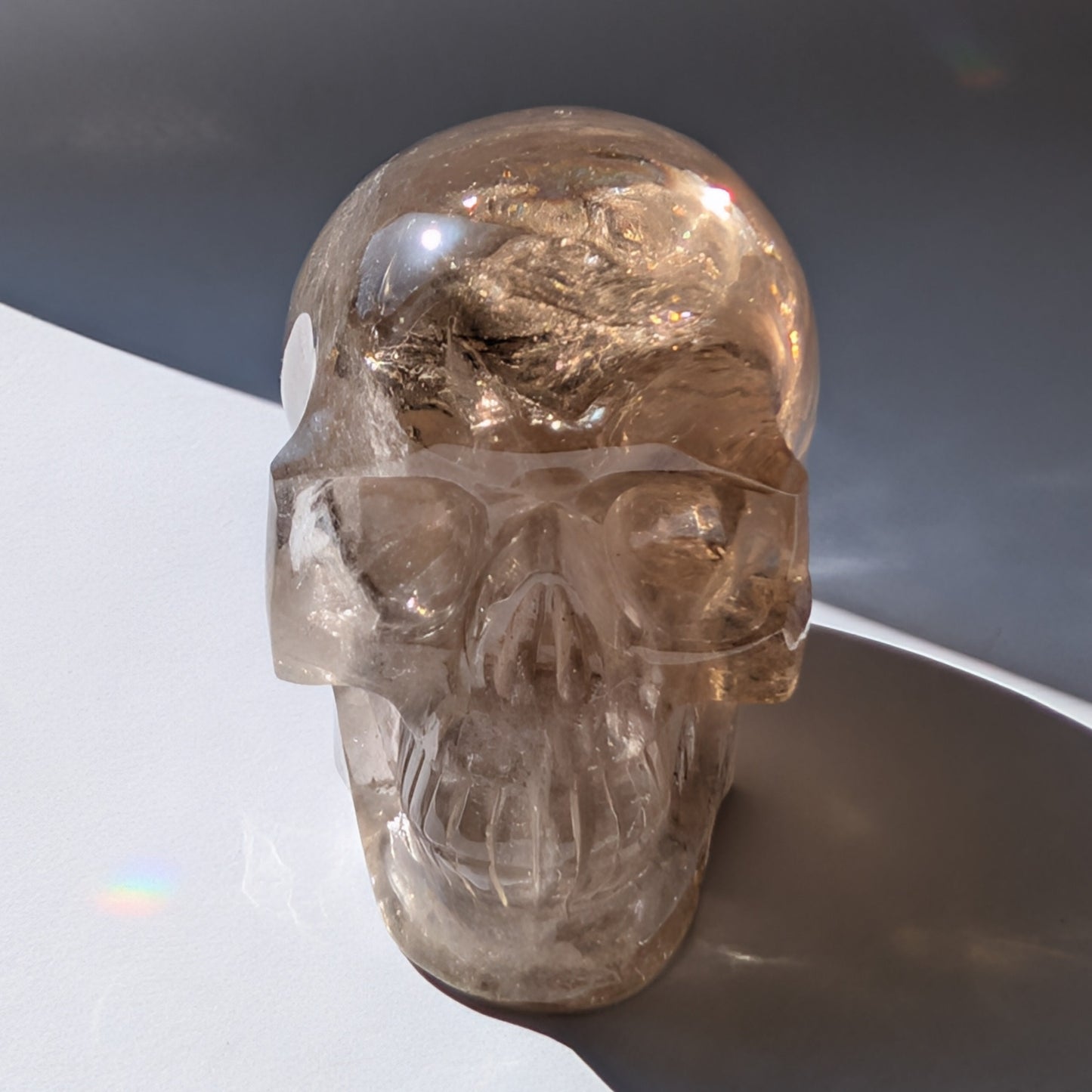Ein 594g schwerer, klarer Rauchquarz-Schädel 'Der Wächter der Schatten' mit leuchtenden Regenbogen-Einschlüssen.