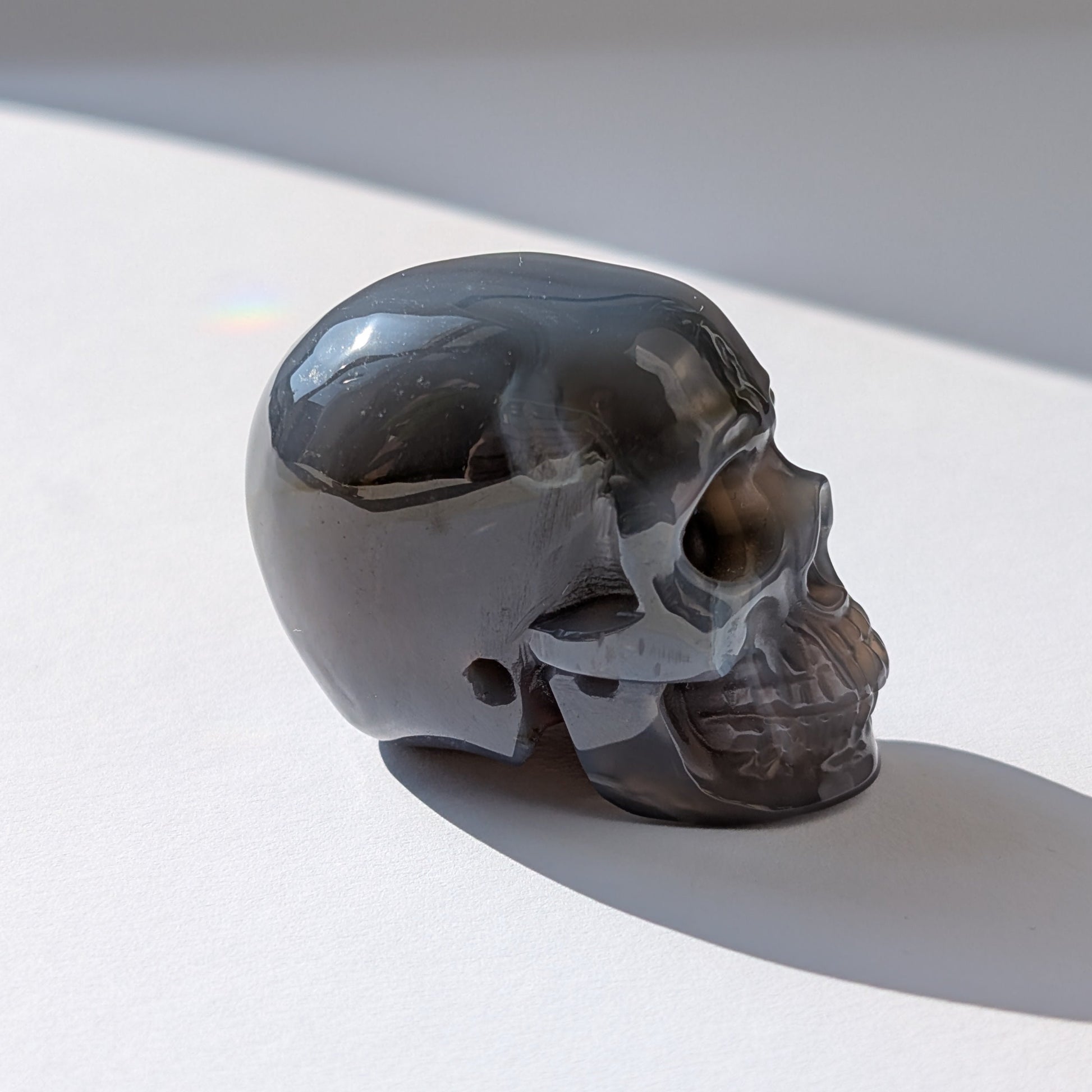Ein 86g schwerer Kristallschädel 'Der Wächter der zwei Welten' aus Gebändertem Achat, dessen eine Hälfte eine offene, funkelnde Druzy-Geode ist.