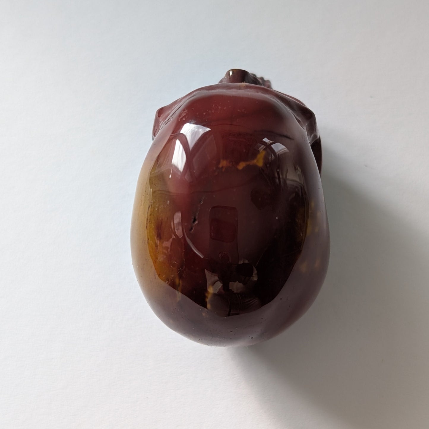 Ein 86g schwerer, handgeschnitzter Kristallschädel 'Wetzlin' aus Mookait mit einer einzigartigen Maserung in erdigen Rot- und Gelbtönen.