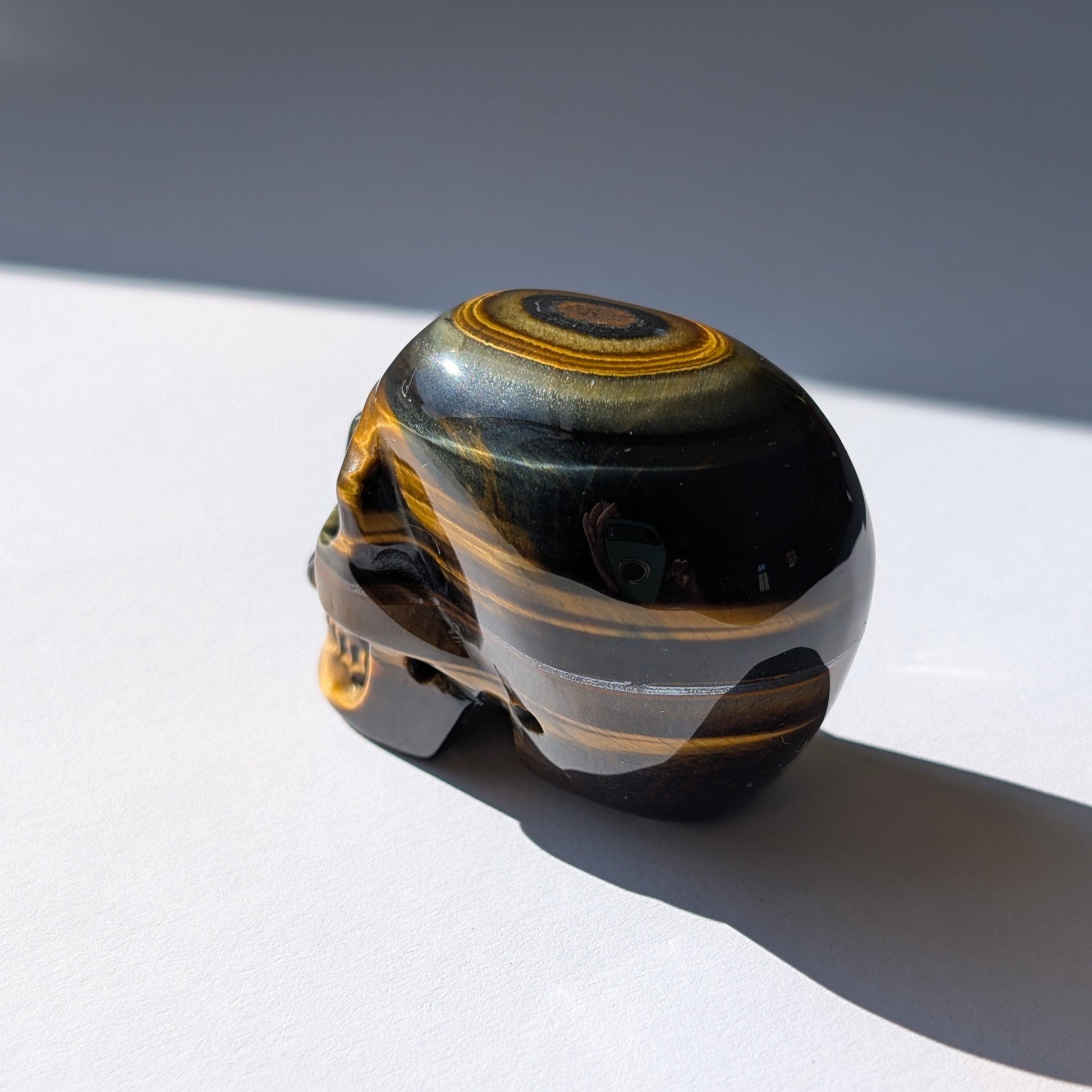 Ein 92g schwerer Kristallschädel 'Erlin' aus Blau-Gold Tigerauge mit einem perfekt geformten, konzentrischen Auge auf dem Scheitel.