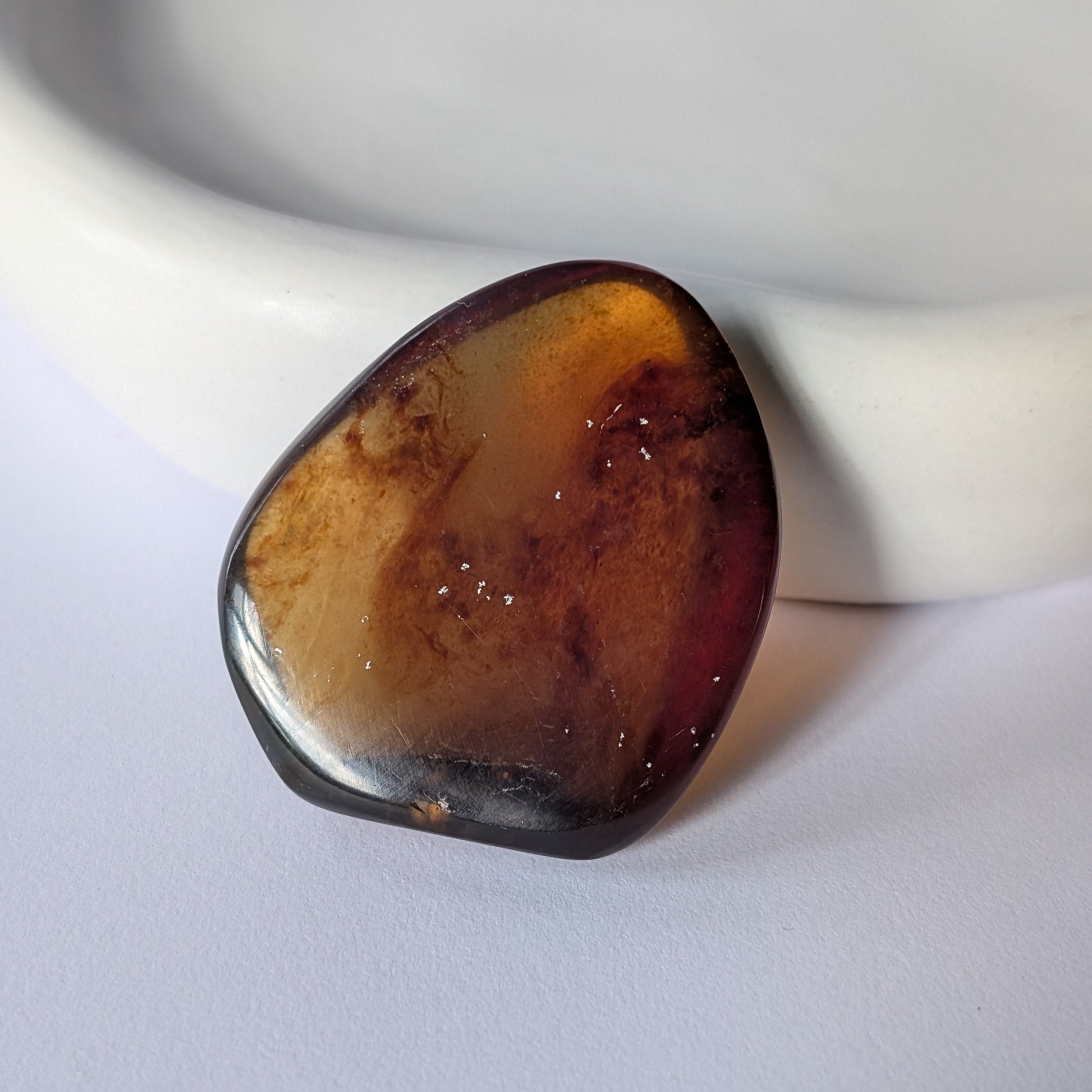 Ein glatt polierter Bicolor-Bernstein 'Funke der Vorzeit', der im Licht von tiefrot zu leuchtend gold schimmert.