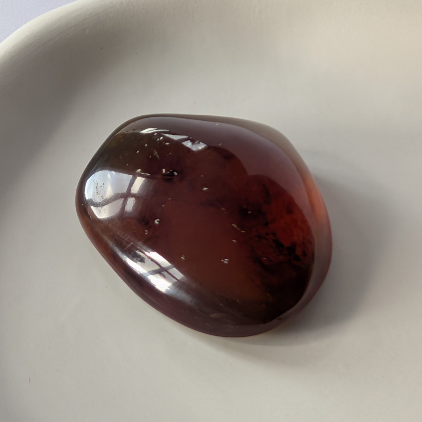 Ein glatt polierter Bicolor-Bernstein 'Funke der Vorzeit', der im Licht von tiefrot zu leuchtend gold schimmert.