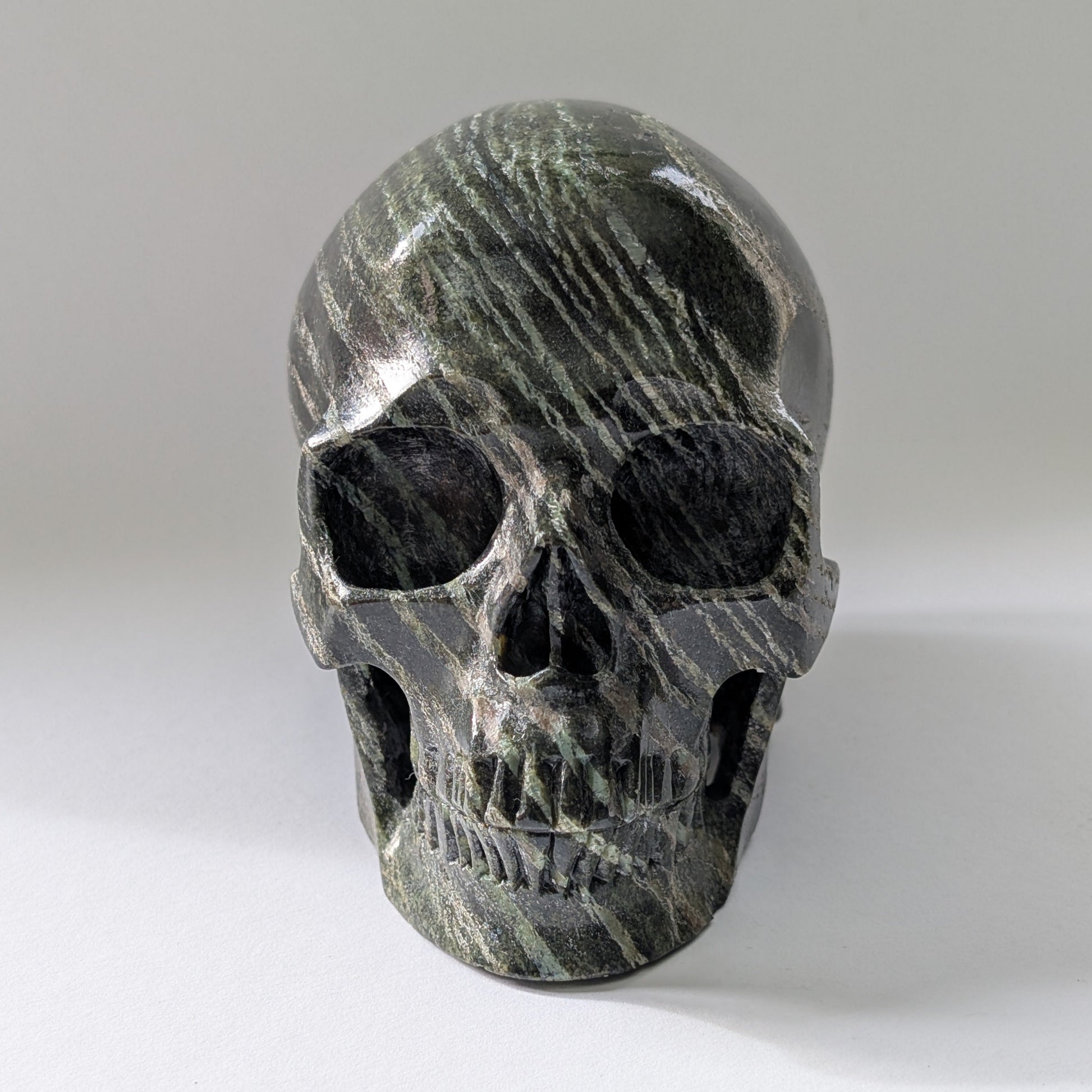 Ein monumentaler, 1204g schwerer Kristallschädel 'Scryer' aus dunkelgrünem Serpentin mit hypnotisierendem, silbrigem Schimmer.