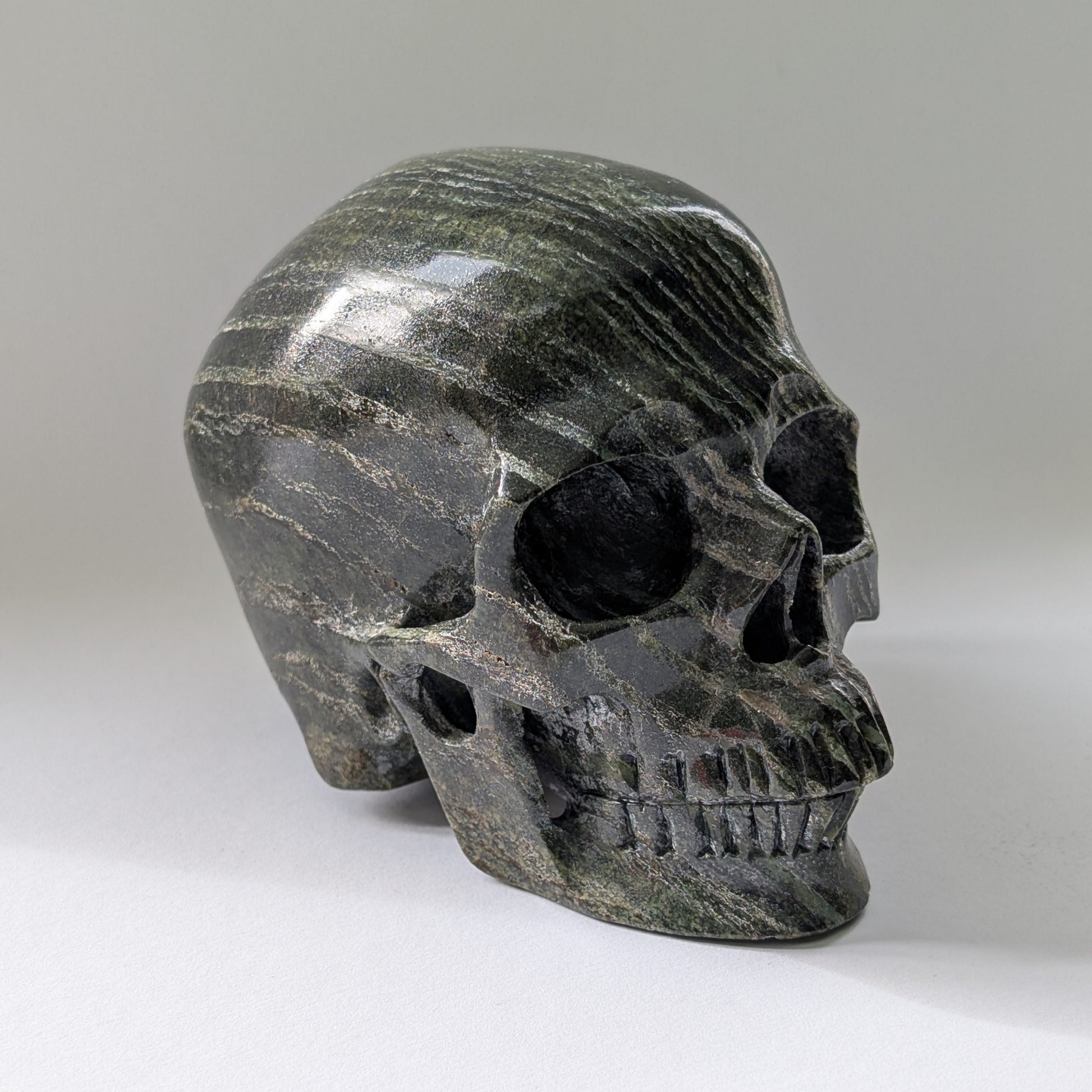 Ein monumentaler, 1204g schwerer Kristallschädel 'Scryer' aus dunkelgrünem Serpentin mit hypnotisierendem, silbrigem Schimmer.